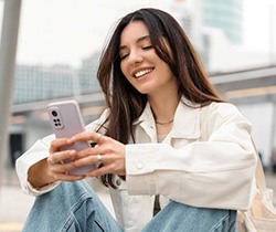Woman smiling while looking at phone outside