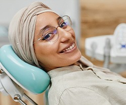 Woman with glasses smiling while sitting in treatment chair