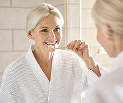 Woman smiling while brushing her teeth in bathroom