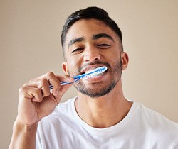 Smiling patient in white shirt brushing their teeth