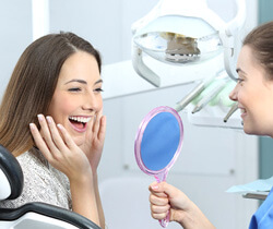 patient smiling at reflection in handheld mirror with dental assistant